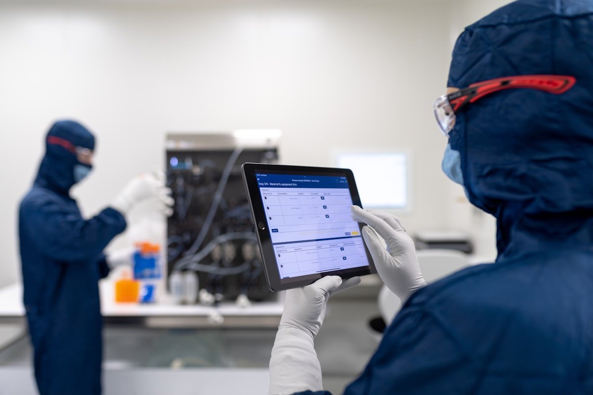 Técnica con equipo de protección consultando un tablero en una tablet dentro de una sala limpia